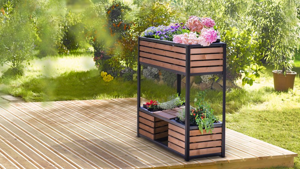 Das Hochbeet 'cube elements' klein steht, bepflanzt mit Blumen und Kräutern, auf einer Holzterrasse im Garten.